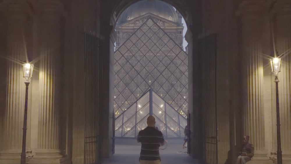 The Louvre pyramid framed by an archway at night straight out of camera in flat Apple Log